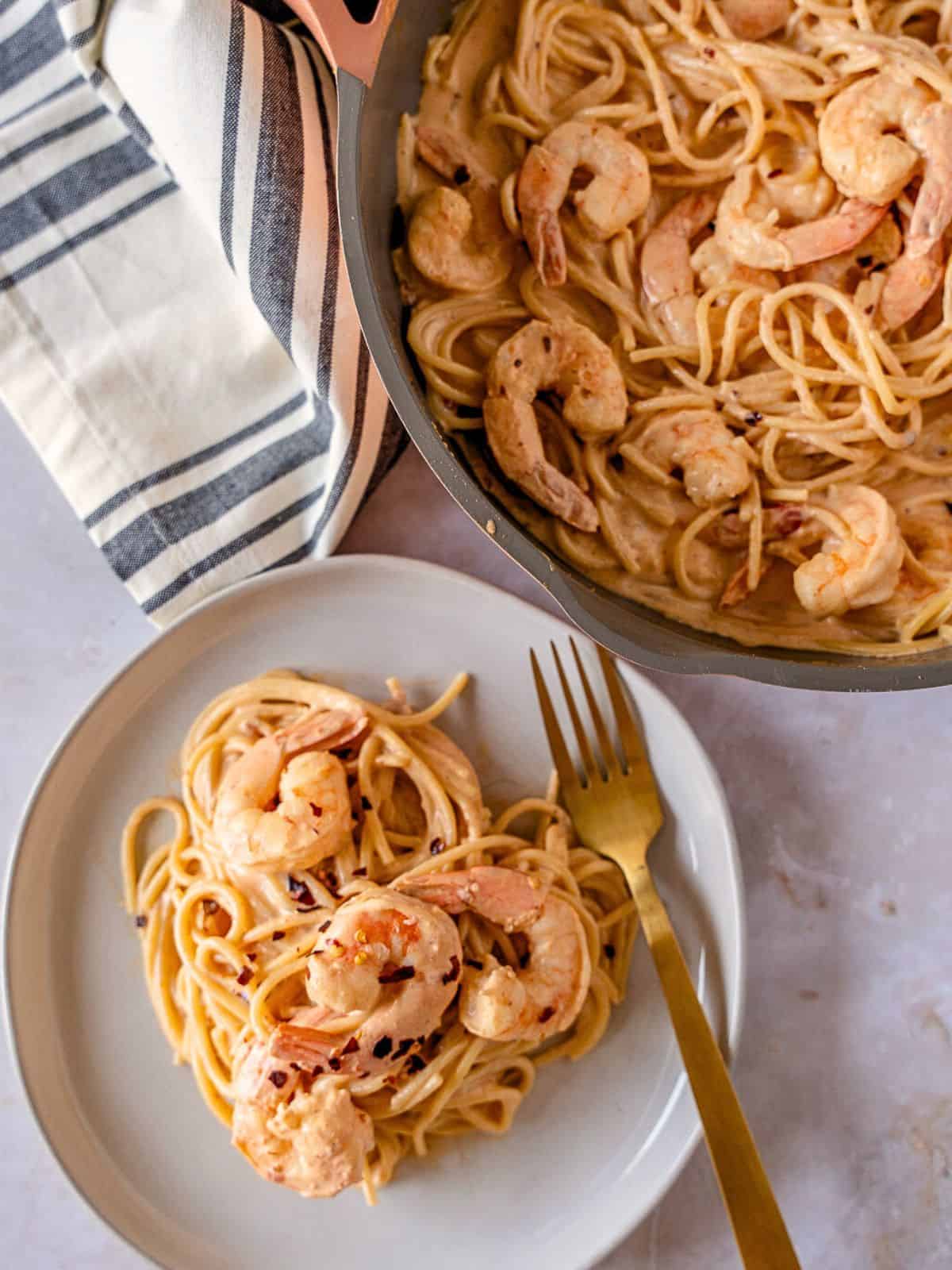 One plate of pasta with shrimp and a skillet with more spicy creamy pasta.