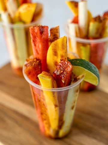 Three Mexican fruit cups topped with chamoy and tajin.