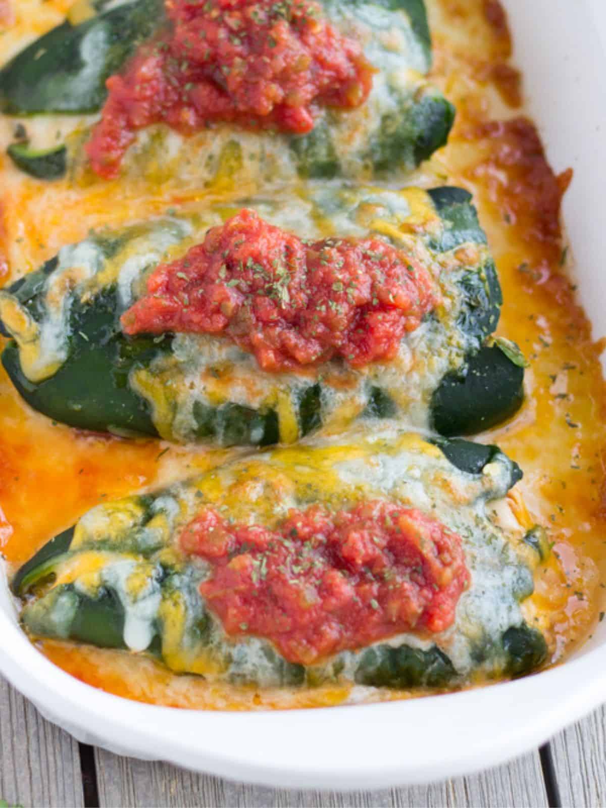Casserole dish with 3 poblano peppers covered with cheese and salsa.