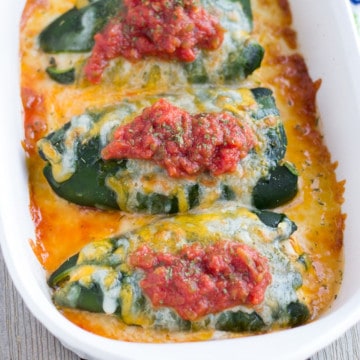 Three chili rellenos in a dish covered in baked cheese and salsa.