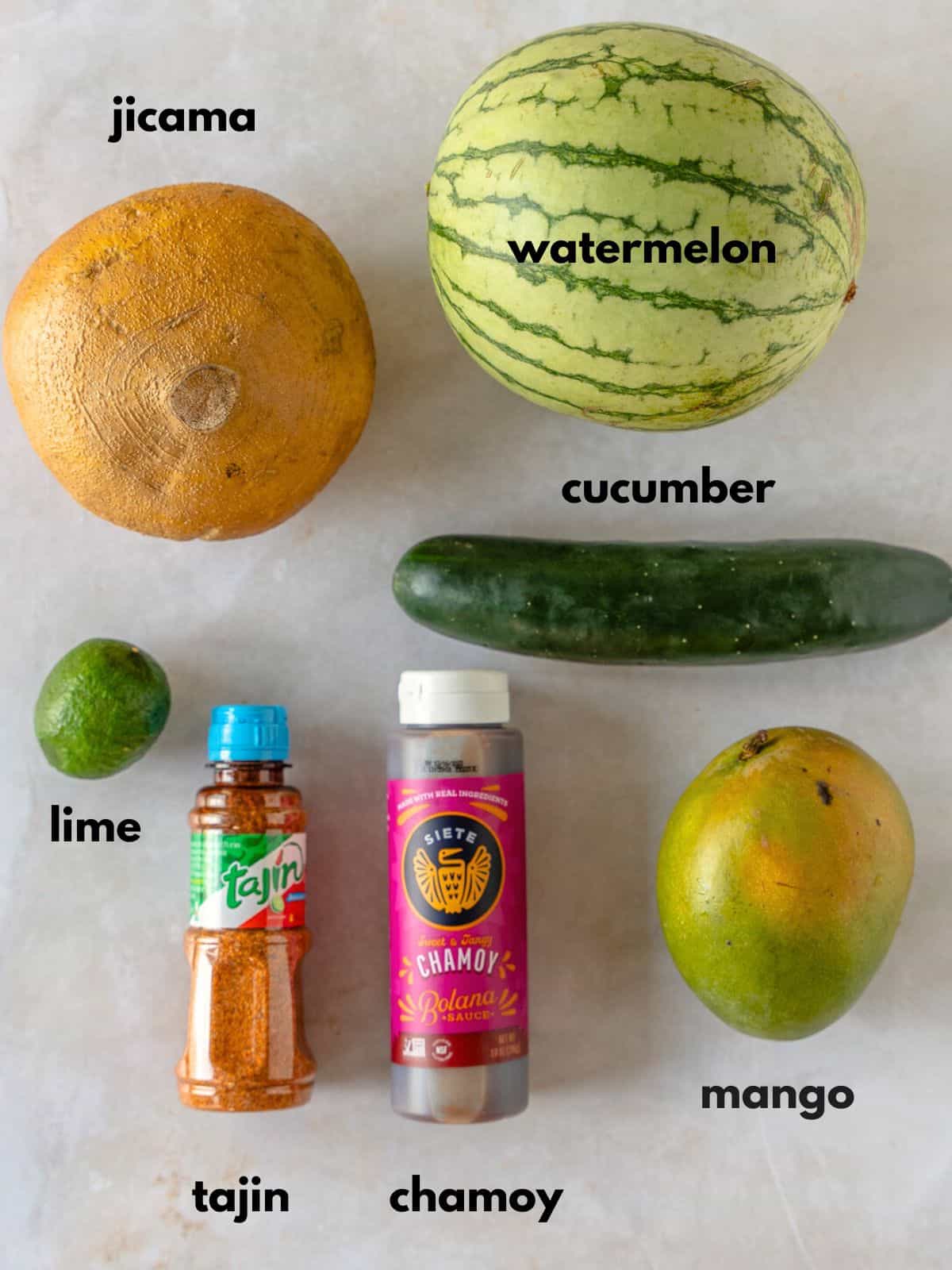 Text labeling the ingredients, jicama, watermelon, cucumber, lime, tajin, chamoy, and mango.