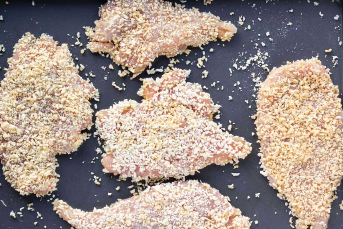Uncooked chicken covered with panko on a baking sheet.