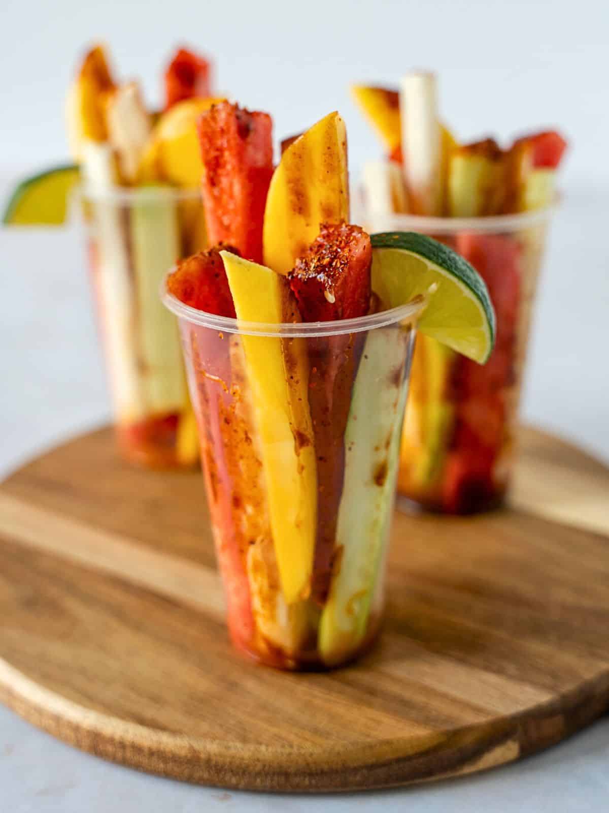 Sliced fruit in a plastic cup topped with chili lime salt and a lime wedge.
