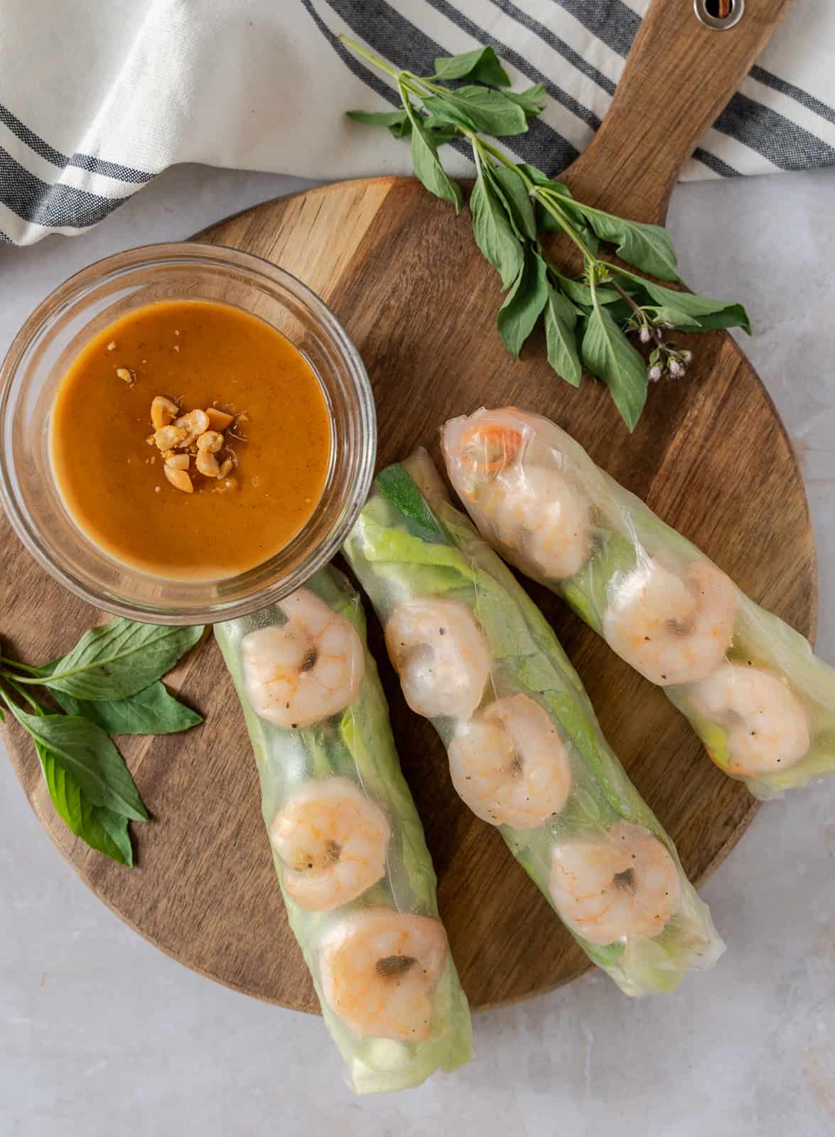 Overhead view of 3 rice paper rolls on a round board with a small bowl of peanut dipping sauce.