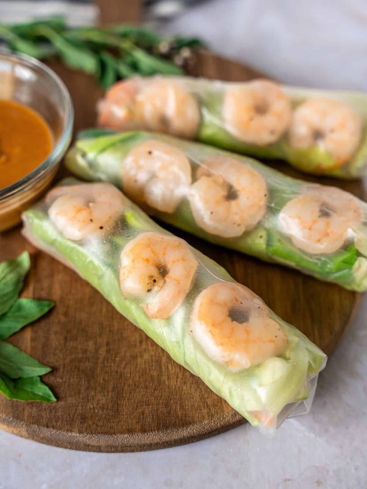 Three rice paper rolls on a wooden board with basil garnish.
