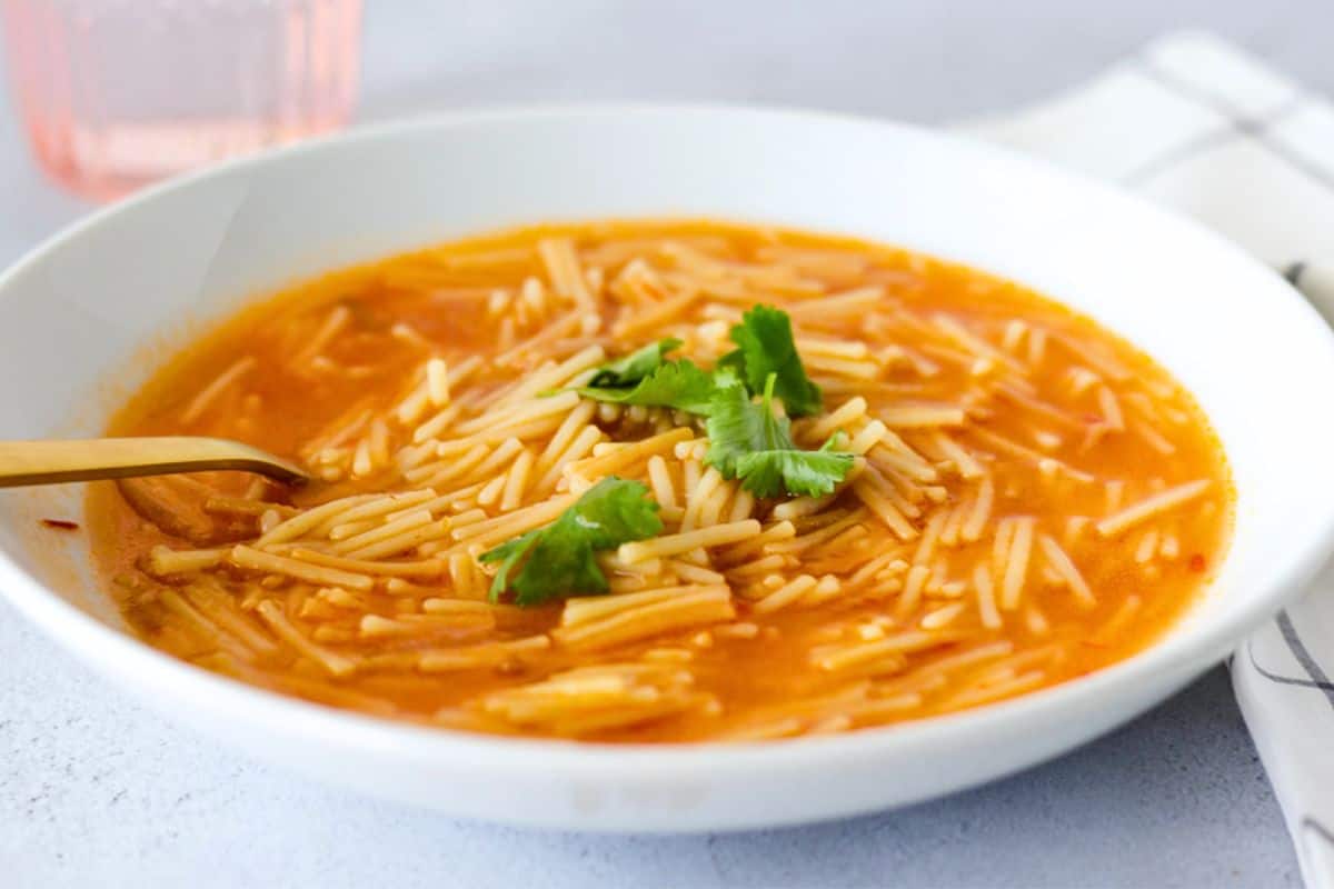 Sopa de fideo in a white bowl with a gold spoon and topped with cilantro.