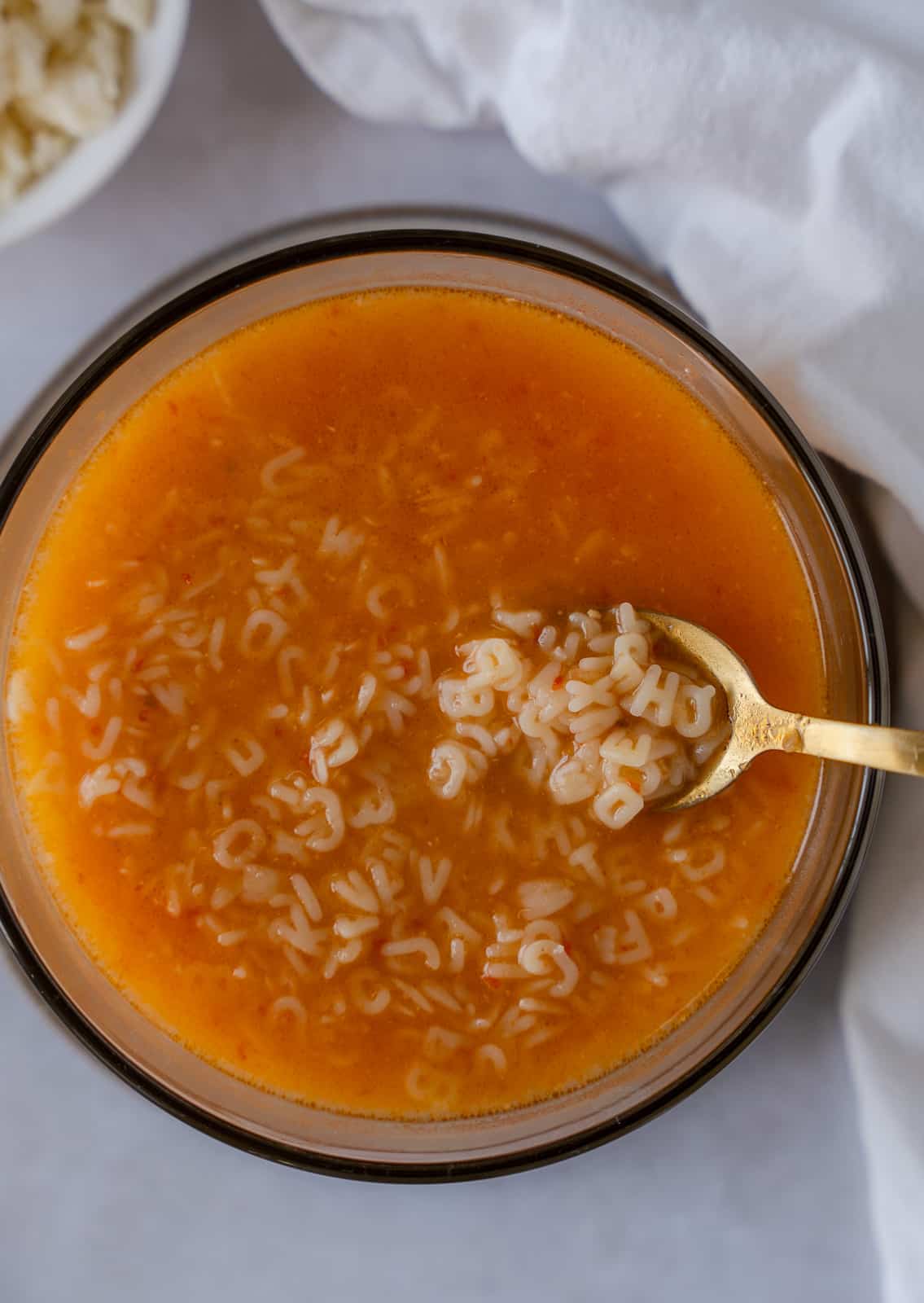 Sopa de Letras in a glass bowl with a gold spoon holding some pasta.