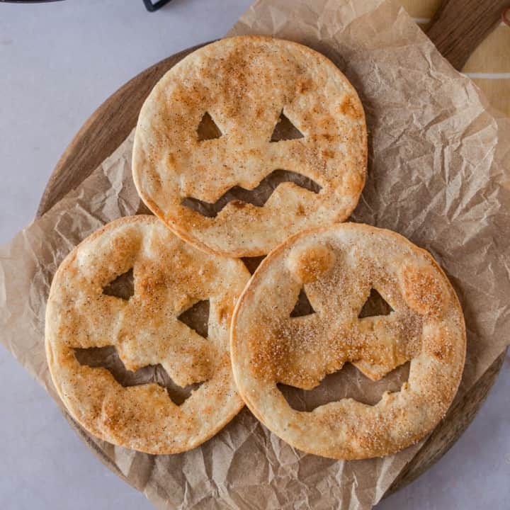 Three cinnamon sugar jack-o-lanterns on a wood board with parchment paper.