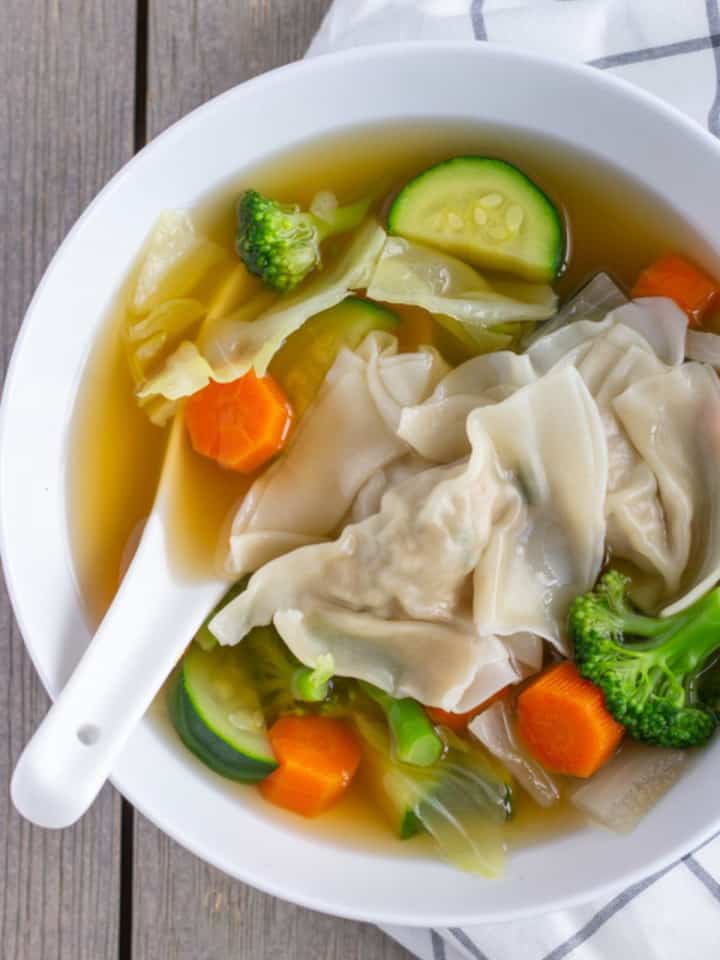 Wonton soup with vegetables in a bowl with a white spoon.