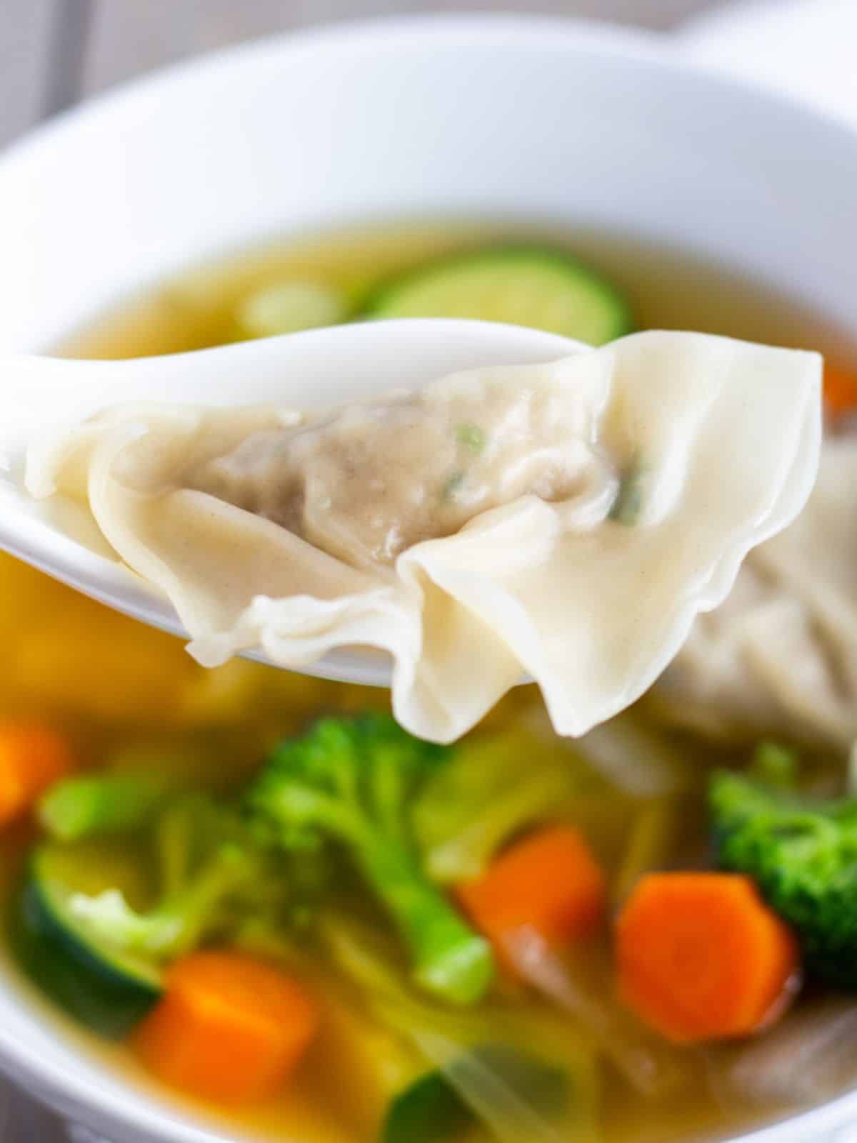 A soup spoon holding a cooked wonton over a bowl of soup.