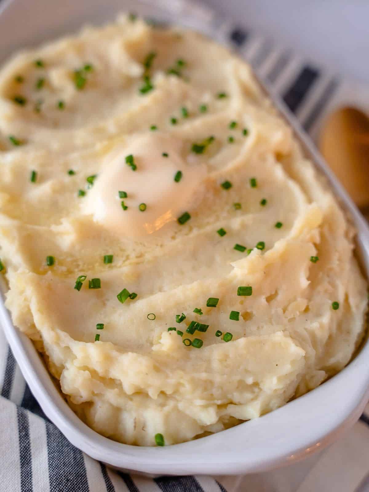 Goat cheese mashed potatoes in a white dish garnished with chives and a pat of butter.