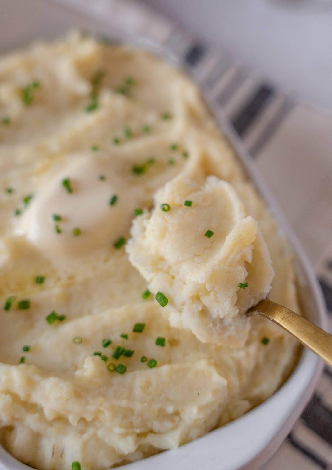 A gold spoon holding some mashed potatoes.