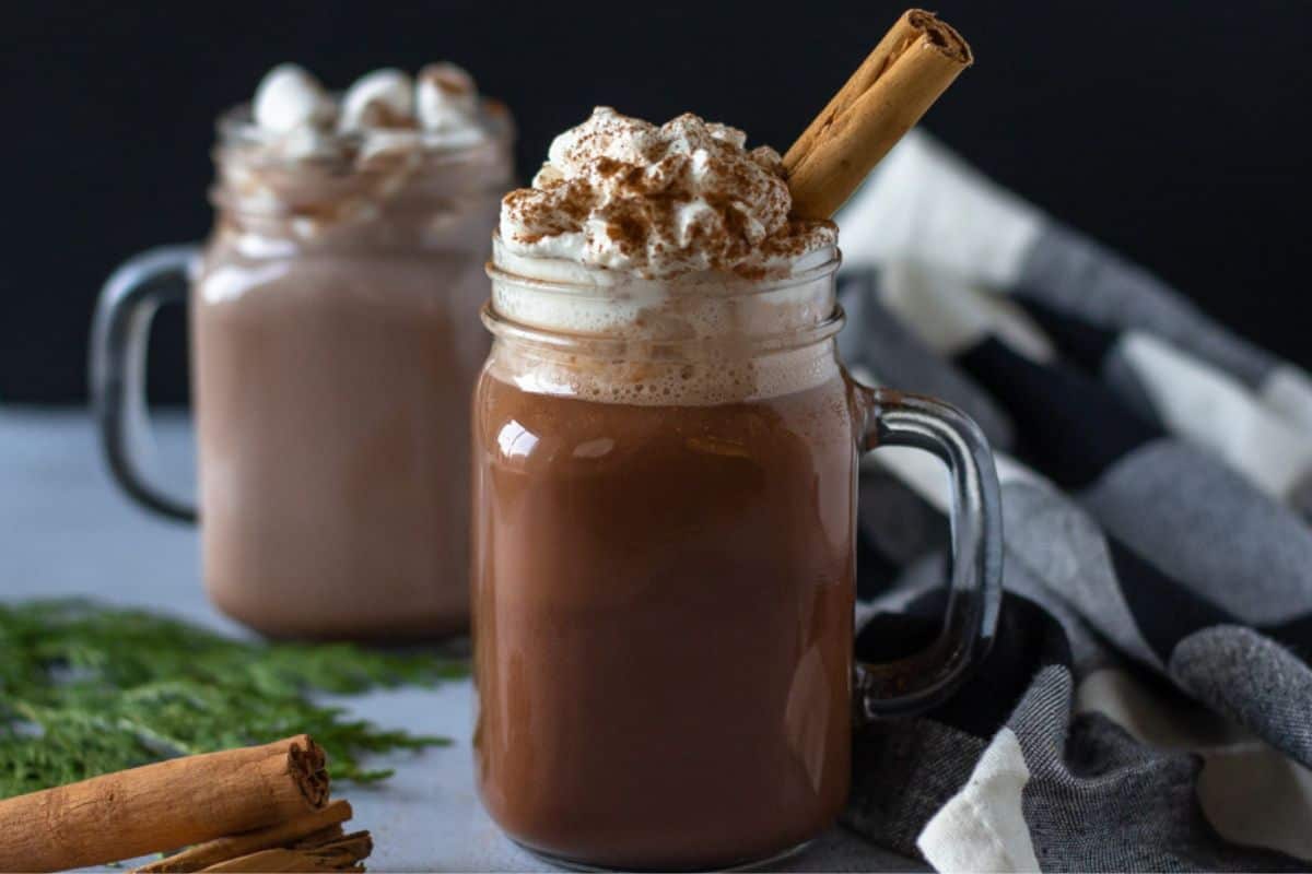Two glass mugs filled with hot cocoa and garnished with whipped cream.