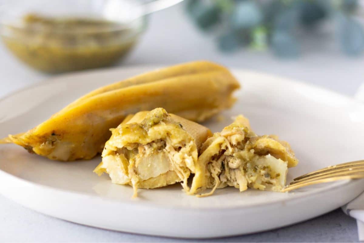 Chicken tamales on a plate with one sliced in half to show filling.