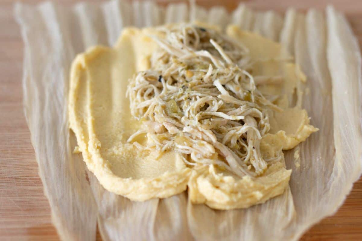 Masa spread out on a corn husk and shredded green chili chicken on top.