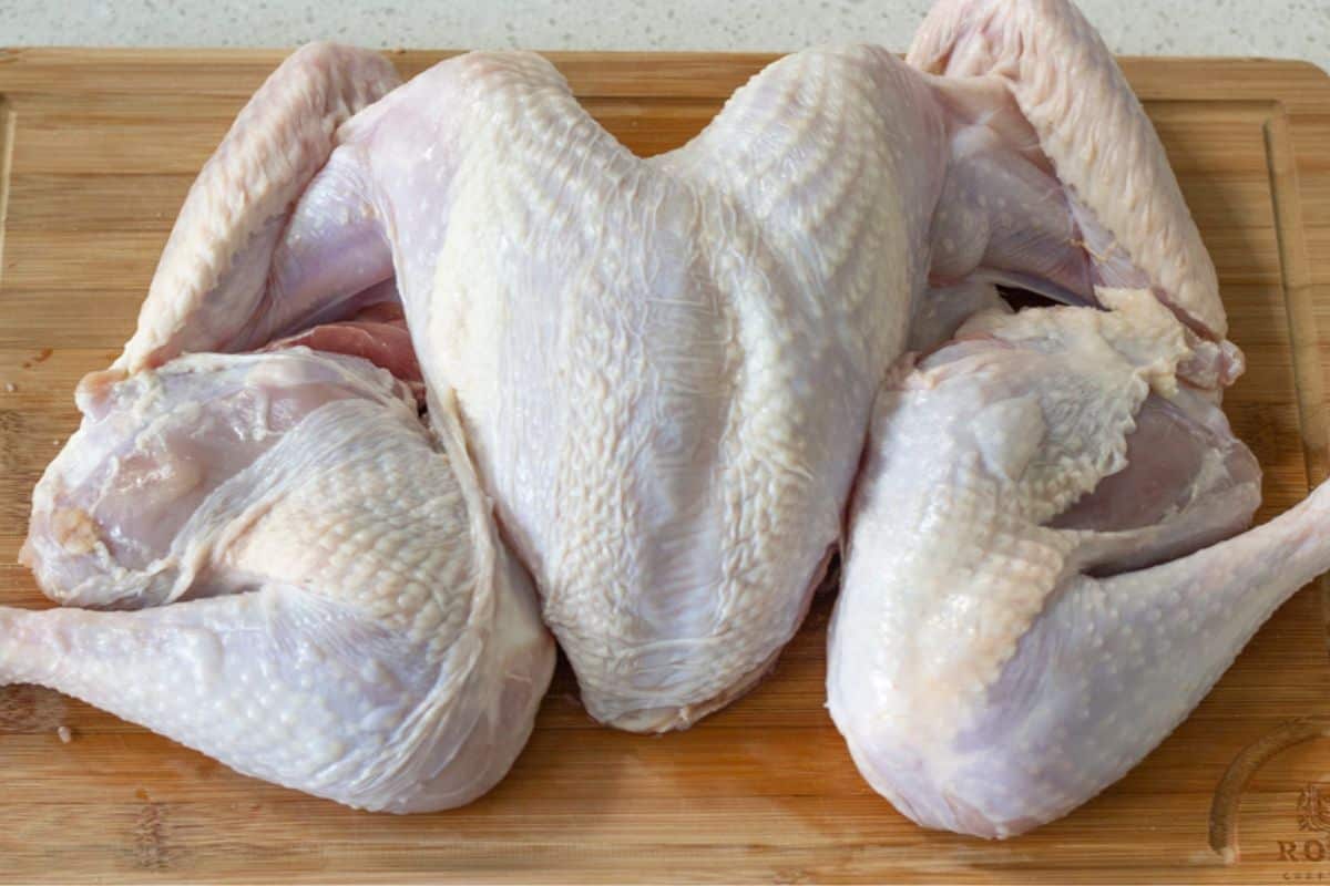A raw spatchcocked turkey on a cutting board.