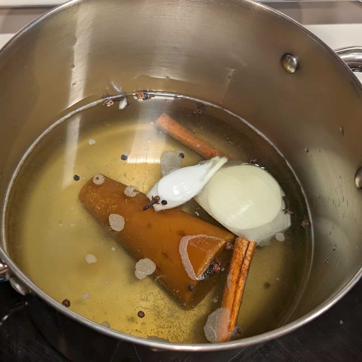 Piloncillo, cinnamon, clove, peppercorns, and a piece of an onion in a pot.