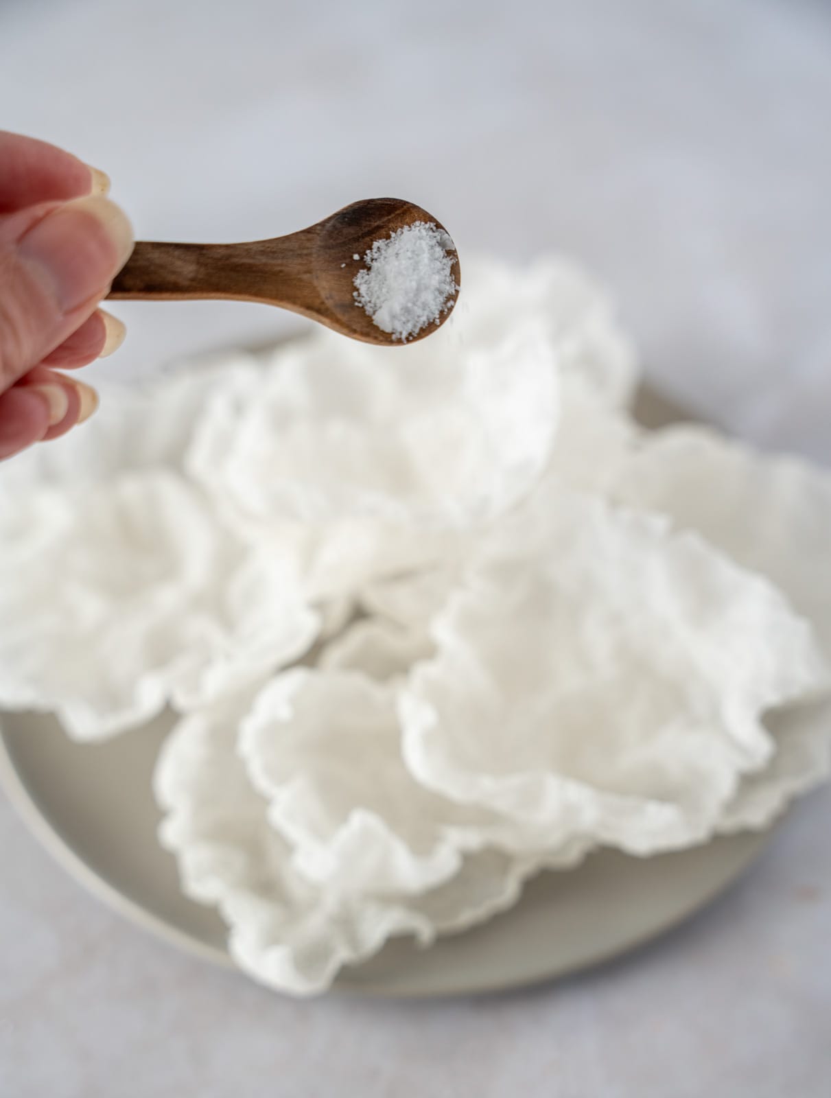 Salt on a wooden spoon being sprinkled onto fried rice paper chips.