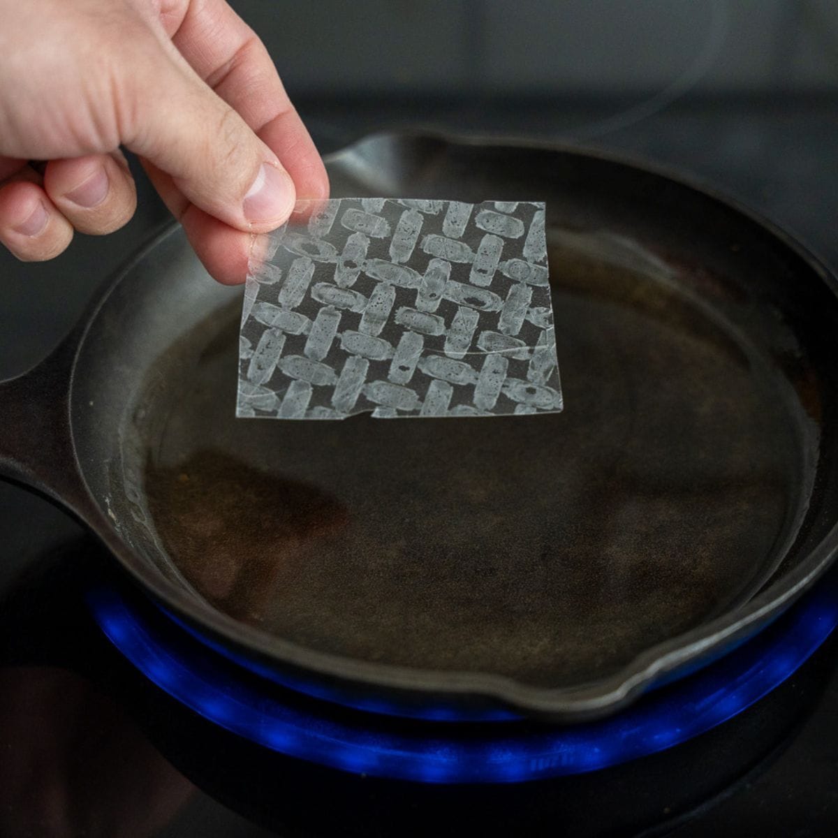 A piece of rice paper being placed into a skillet with hot oil.