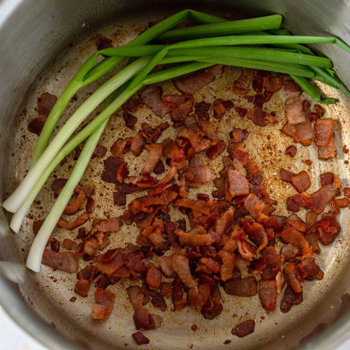 Cooked bacon and green onions in a pot.