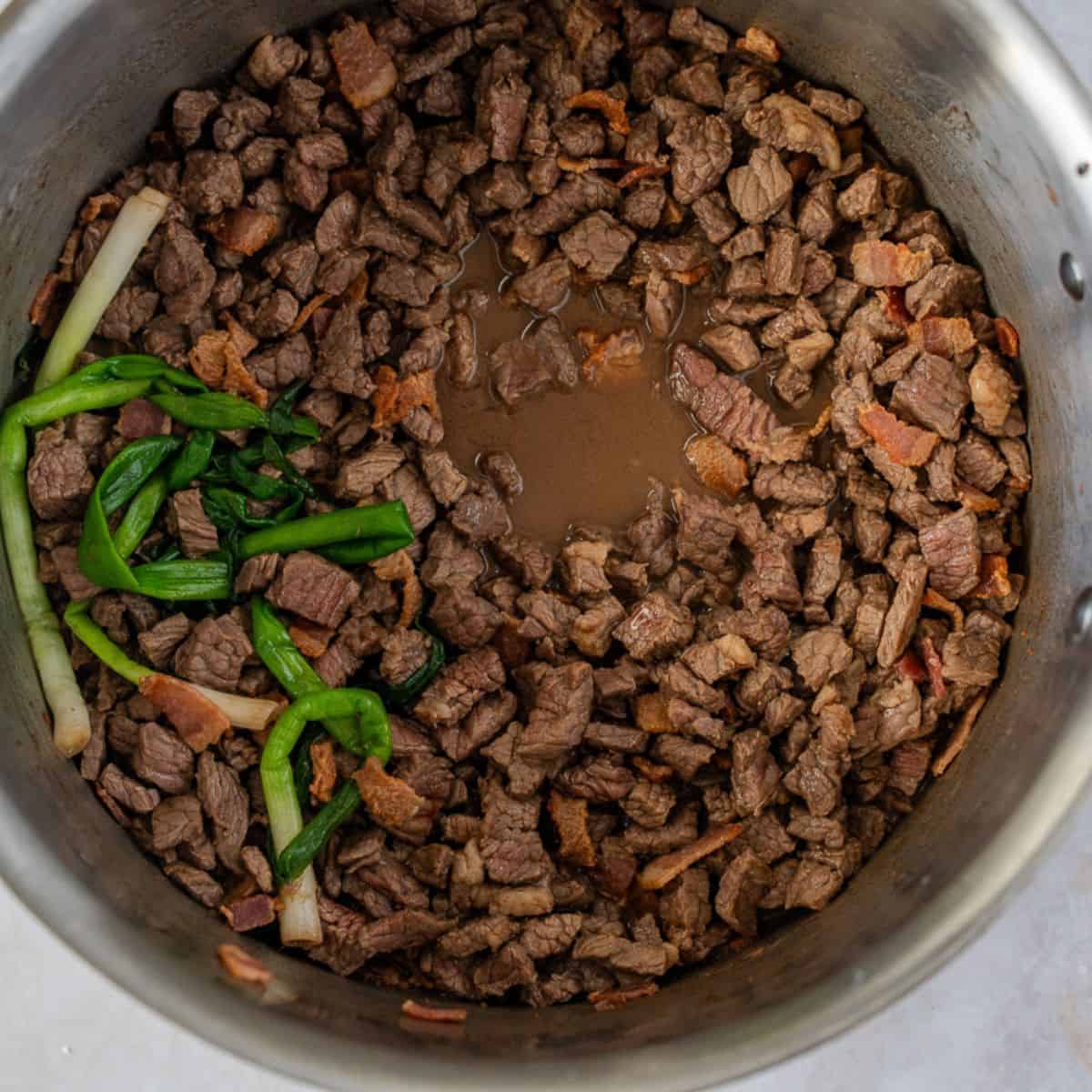Cooked diced beef, bacon, and green onions in a pot.