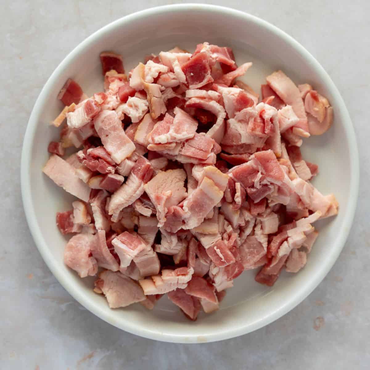 Uncooked diced bacon on a white plate.