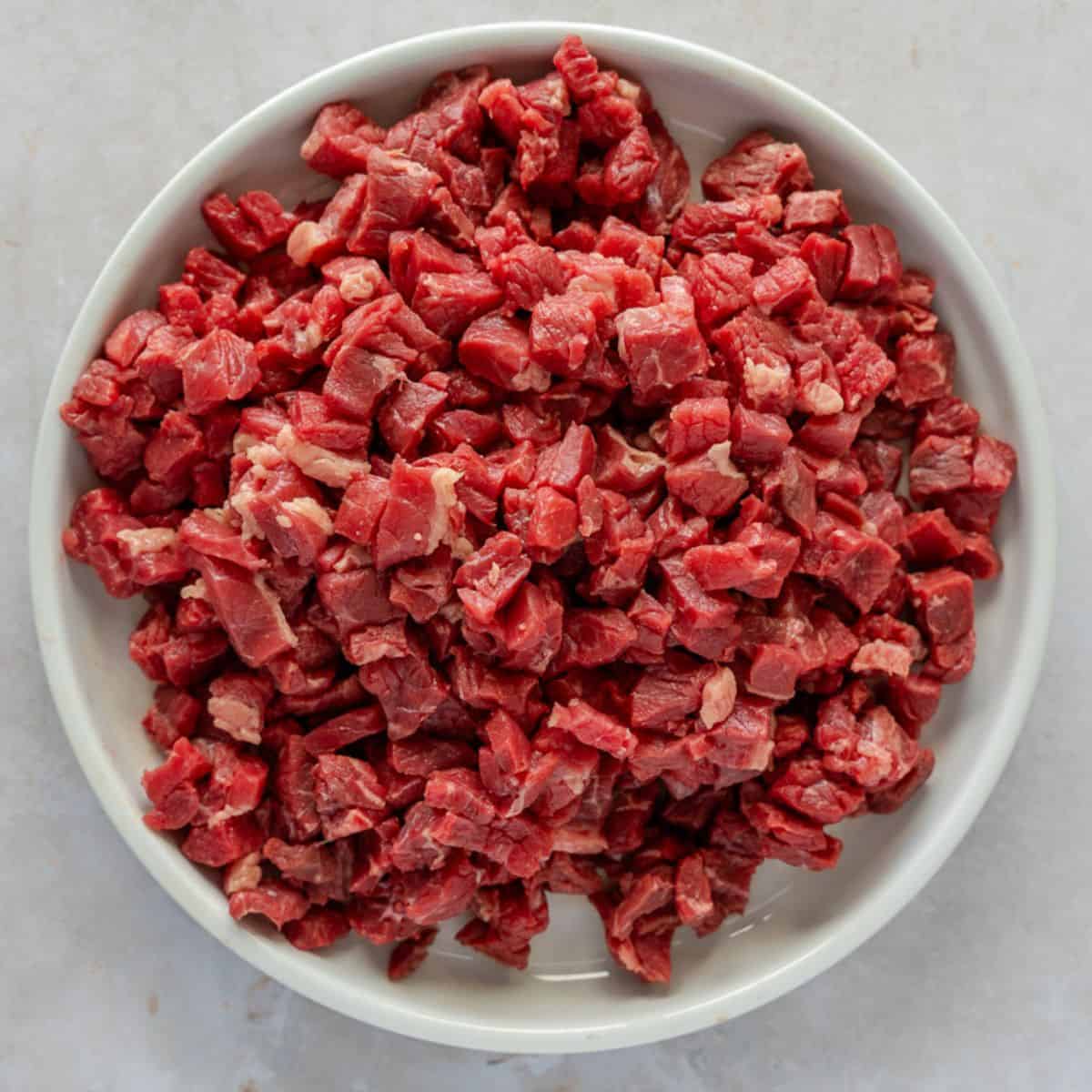 Uncooked diced beef on a round white plate.