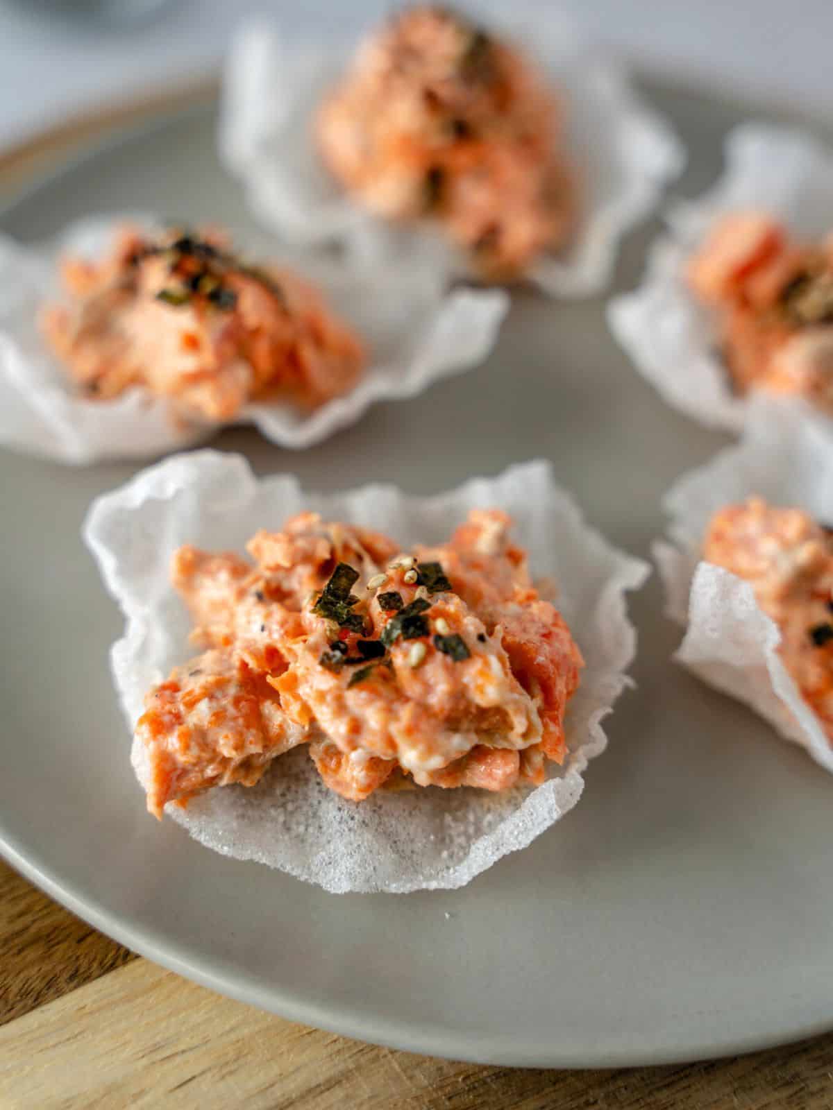 Up close shot of salmon salad on rice paper chips and topped with seaweed.