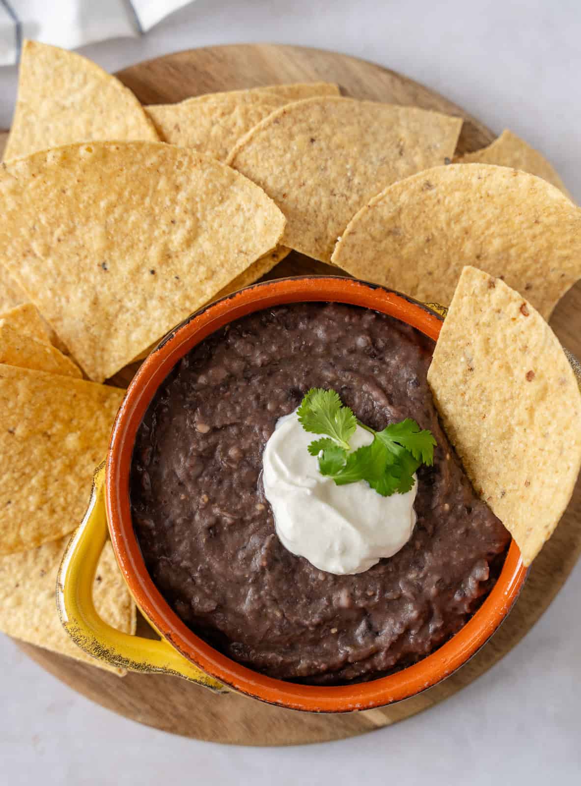 Overhead view of black bean dip on a wooden board with tortilla chips.