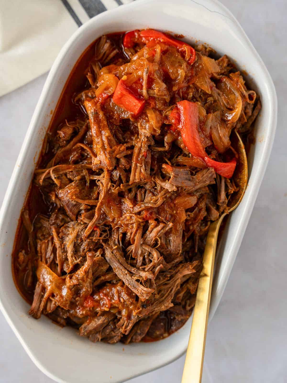 Mexican pot roast in white dish with bell peppers and onions on the side.
