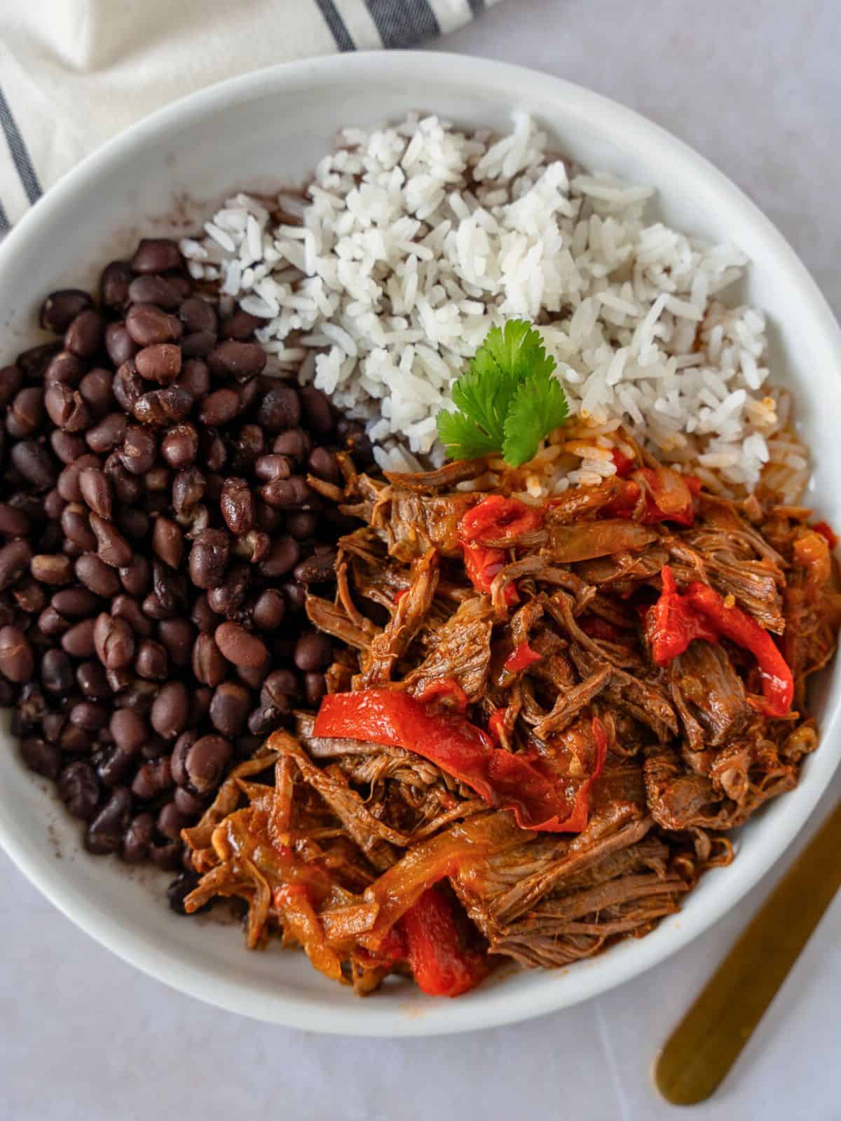 Overhead view of Mexican pot roast on a plate with white rice and black beans.