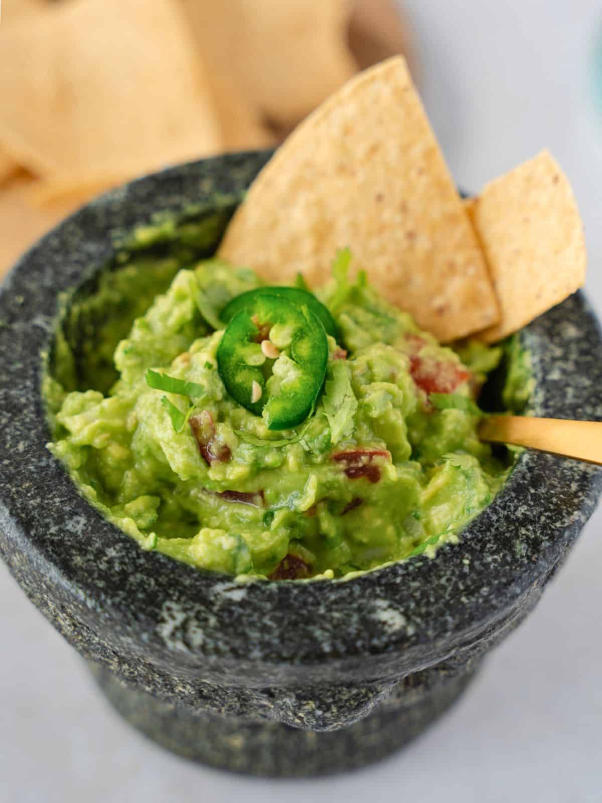 Up close view of guacamole in a molcajete topped with jalapeno slices and tortilla chips.