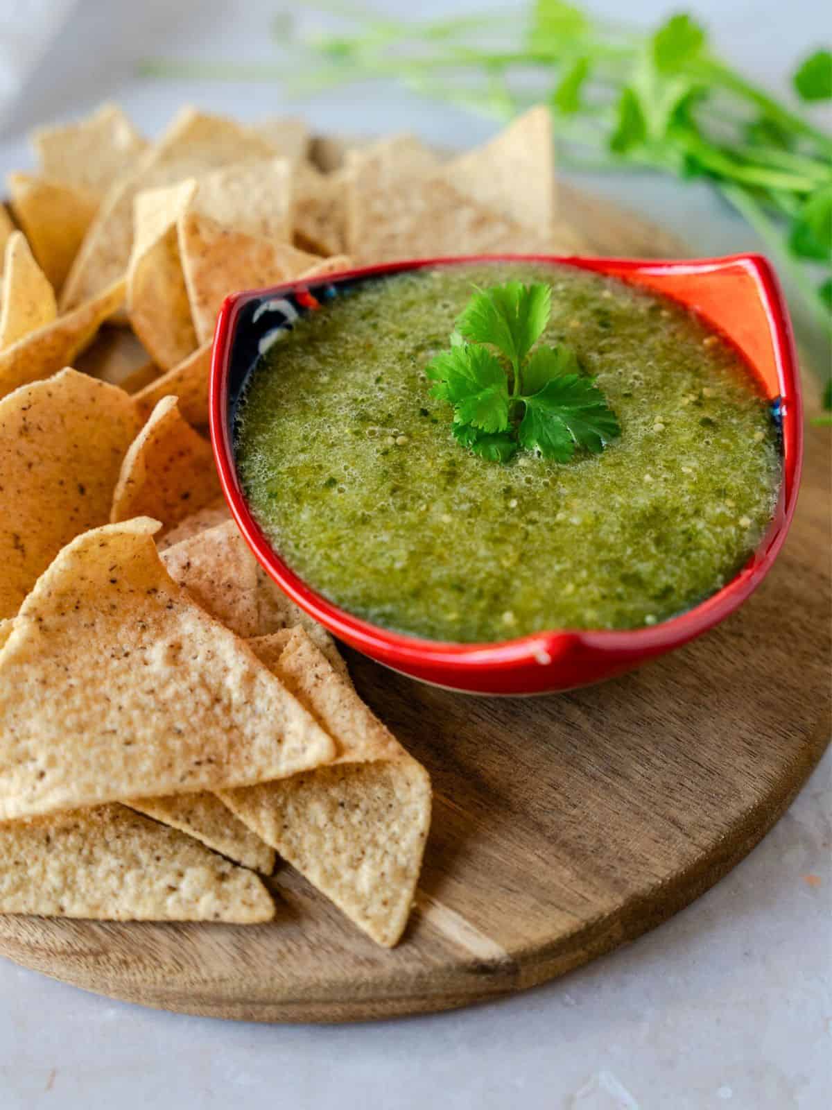 Salsa Verde in a red bowl with tortilla chips on the side.