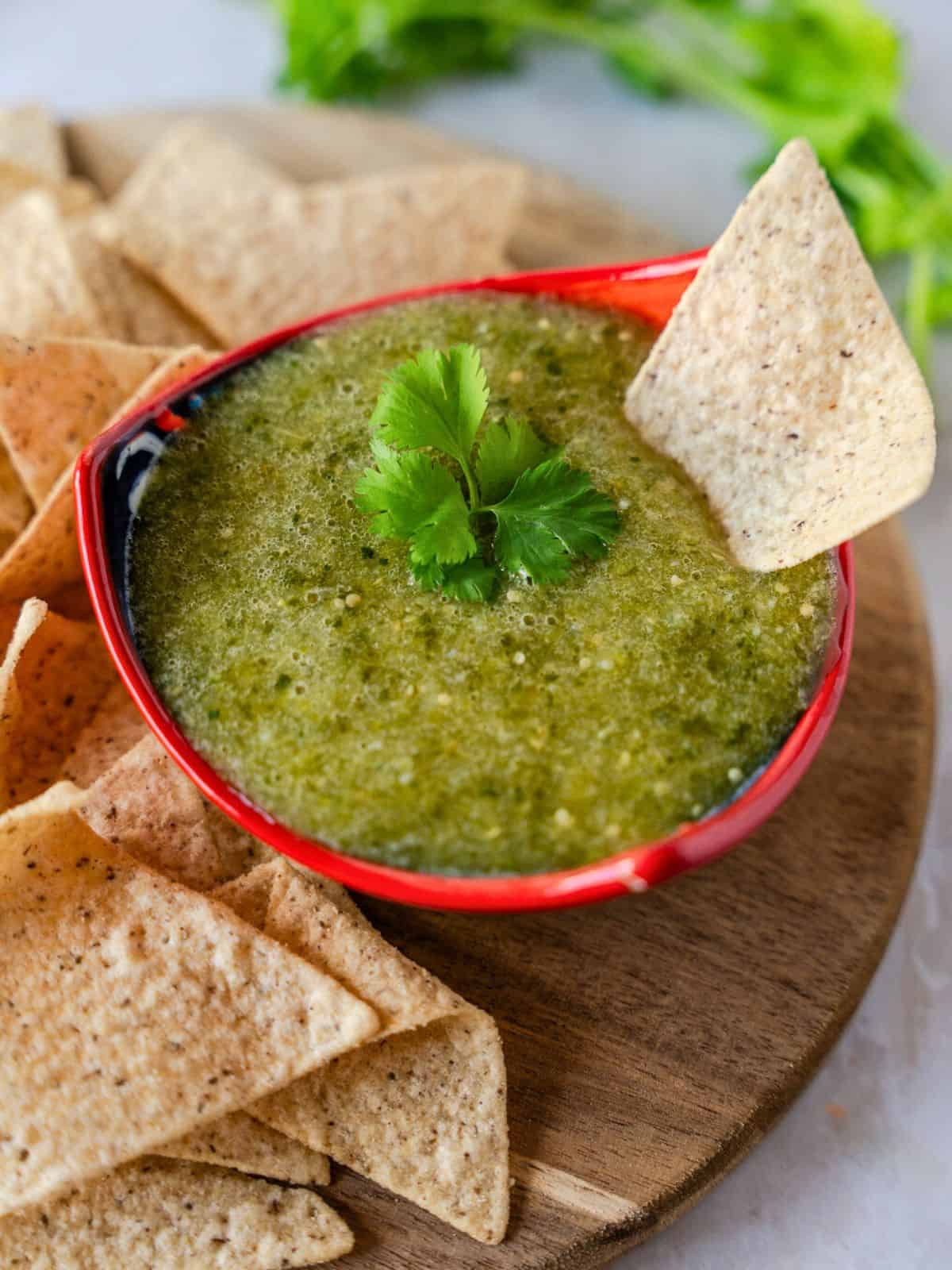 Up close view of salsa verde in a red bowl with a tortilla chip dipped in.
