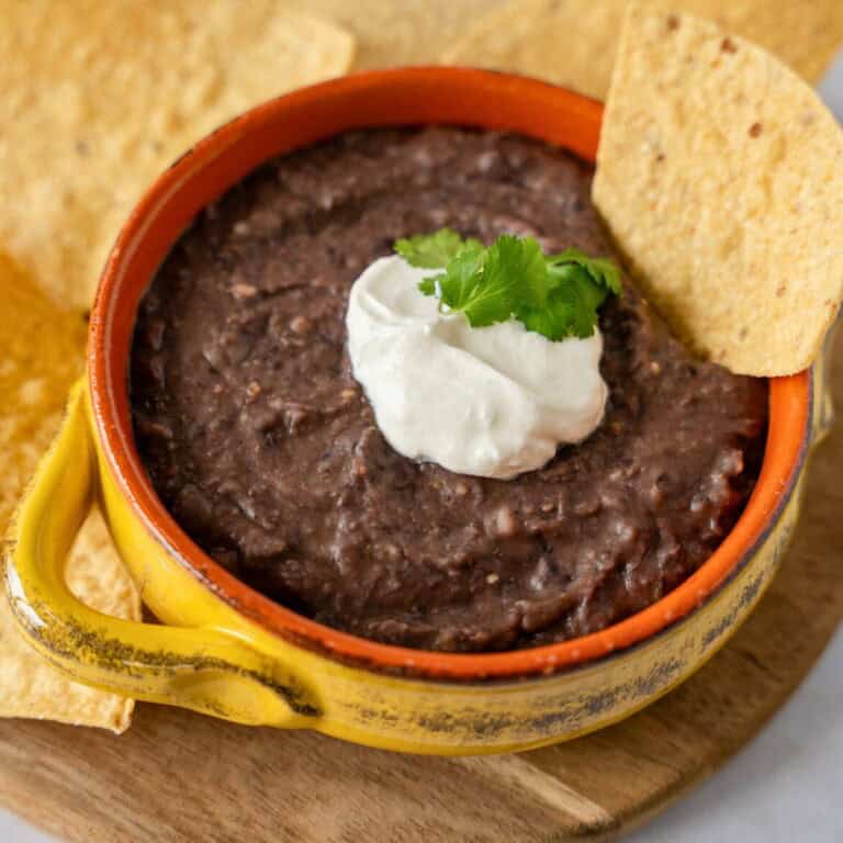 Feature image of black bean dip topped with sour cream in a yellow bowl.