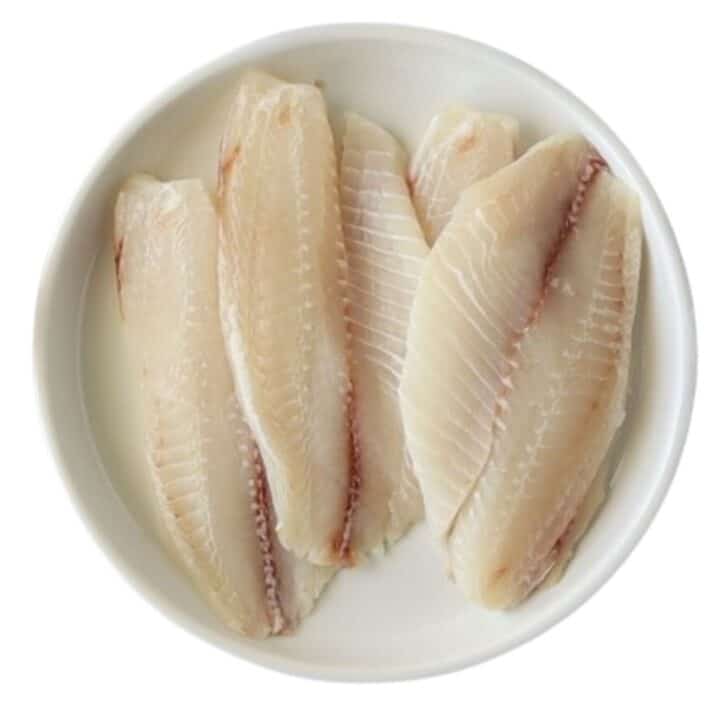 Raw tilapia filets on a white plate.