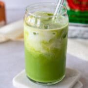Green iced tea in a glass topped with milk.