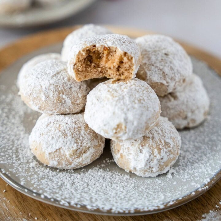 Feature image of Mexican wedding cookies stacked on a plate with one that has a bite taken out.