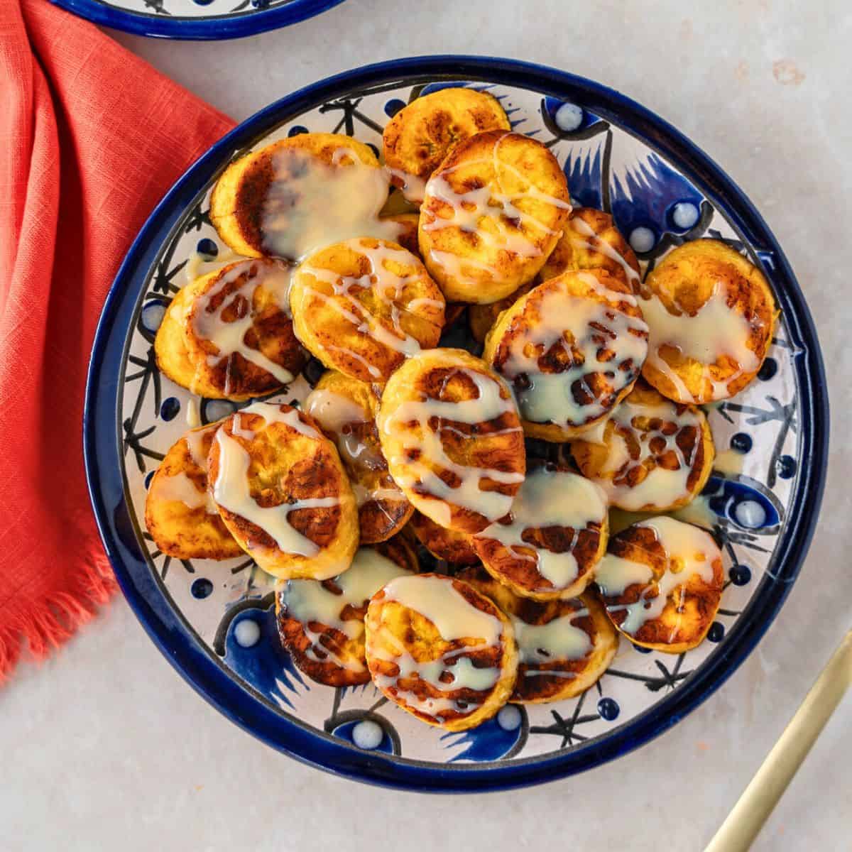 Feature image of Plátanos Fritos with sweetened condensed milk on a blue plate.