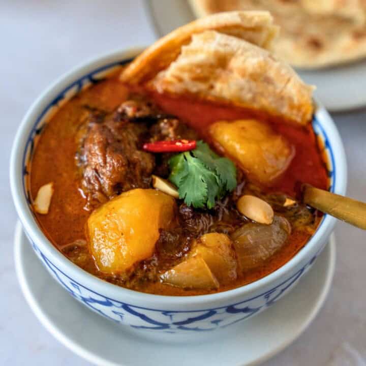 Feature image of massaman beef curry in a bowl with pieces of flatbread inside.