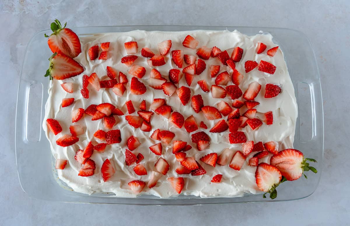 Strawberry tres leches cake in a glass pan with diced strawberries on top.