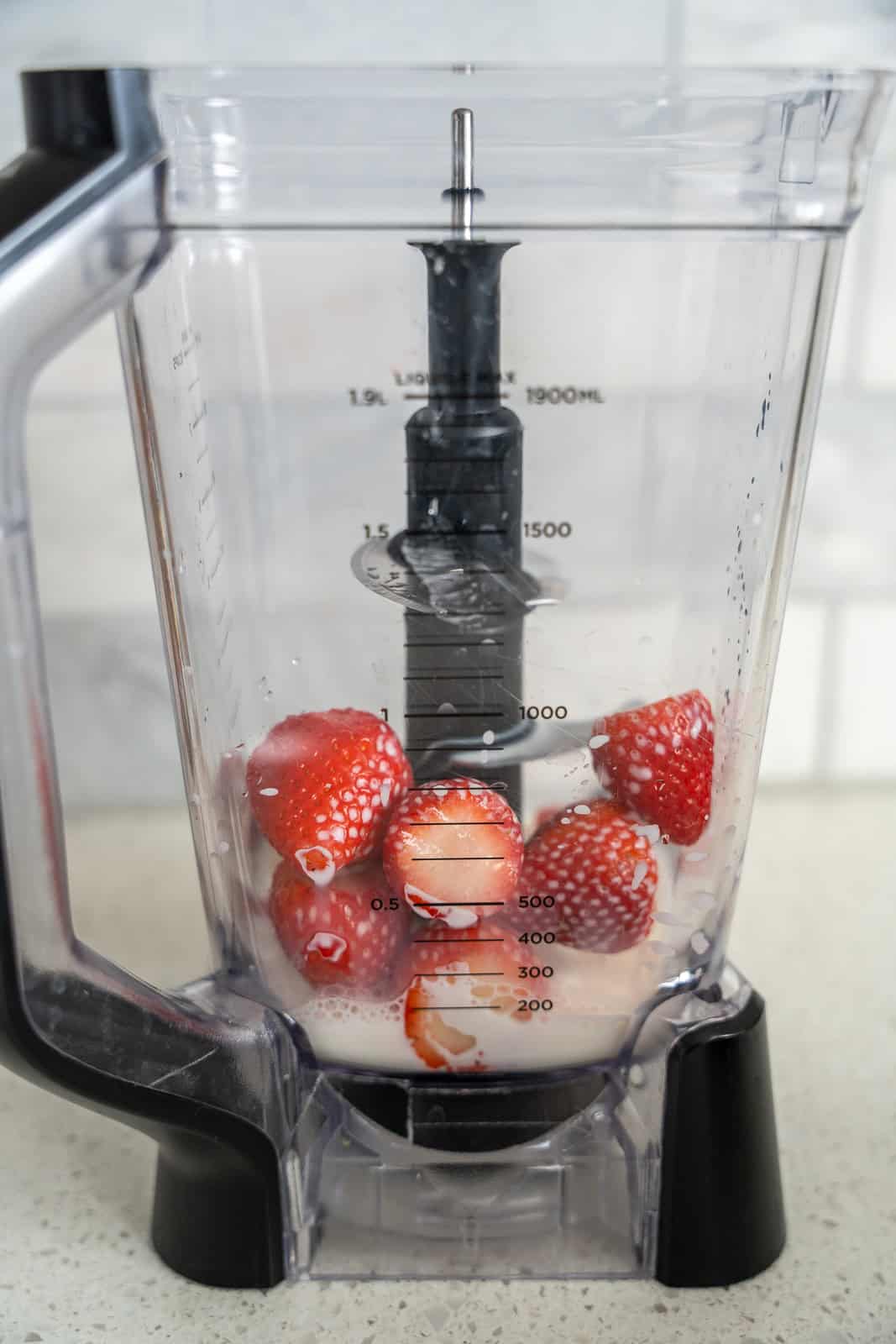 Whole strawberries in a blender with some milk.