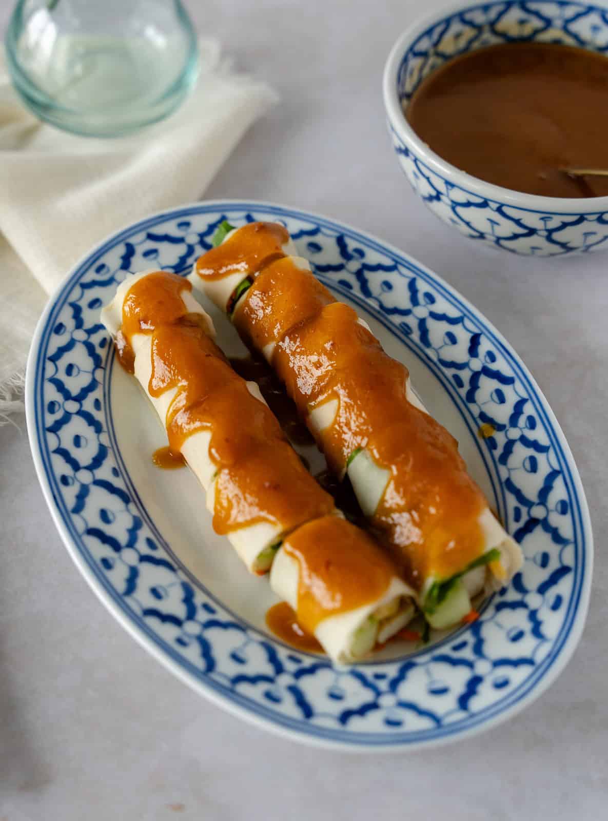 Paw pia sot or Thai fresh spring roll on a blue plate drizzled with a brown sauce.