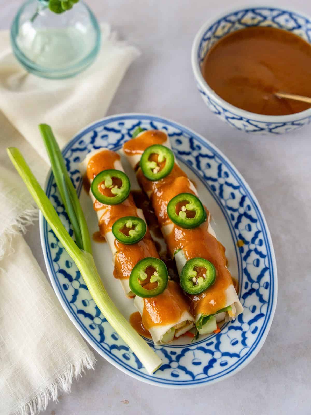 Paw pia sot or Thai fresh spring roll on a blue plate garnished with sliced jalapenos and green onion.