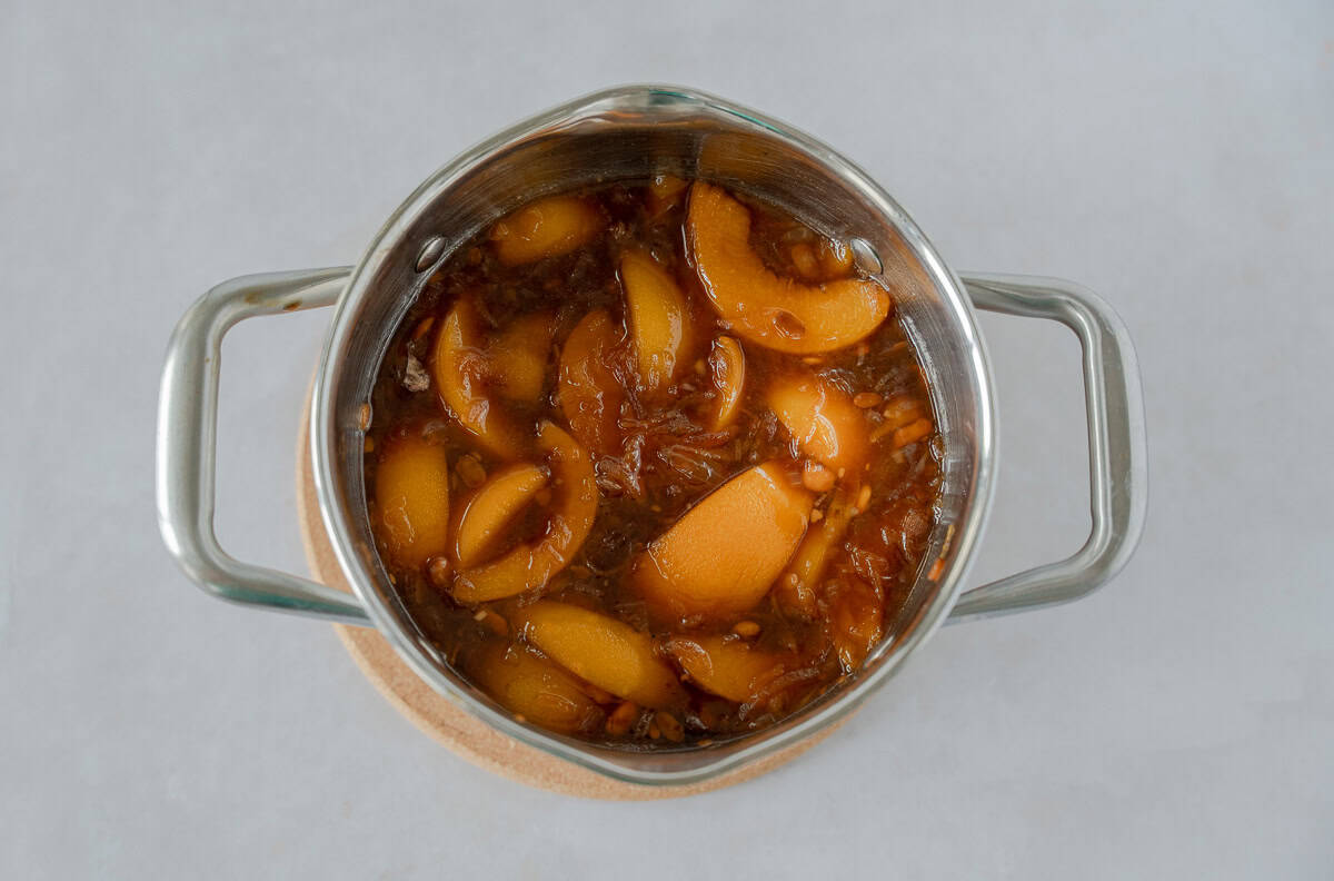 Brown sauce in a pot with sliced peaches on top.