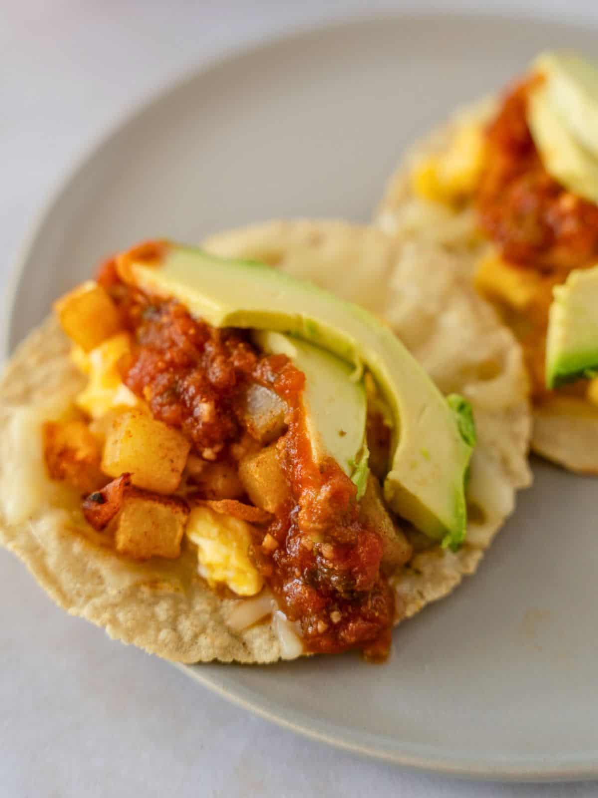 Up close view of potato and egg taco with cheese, salsa, and avocado slices.