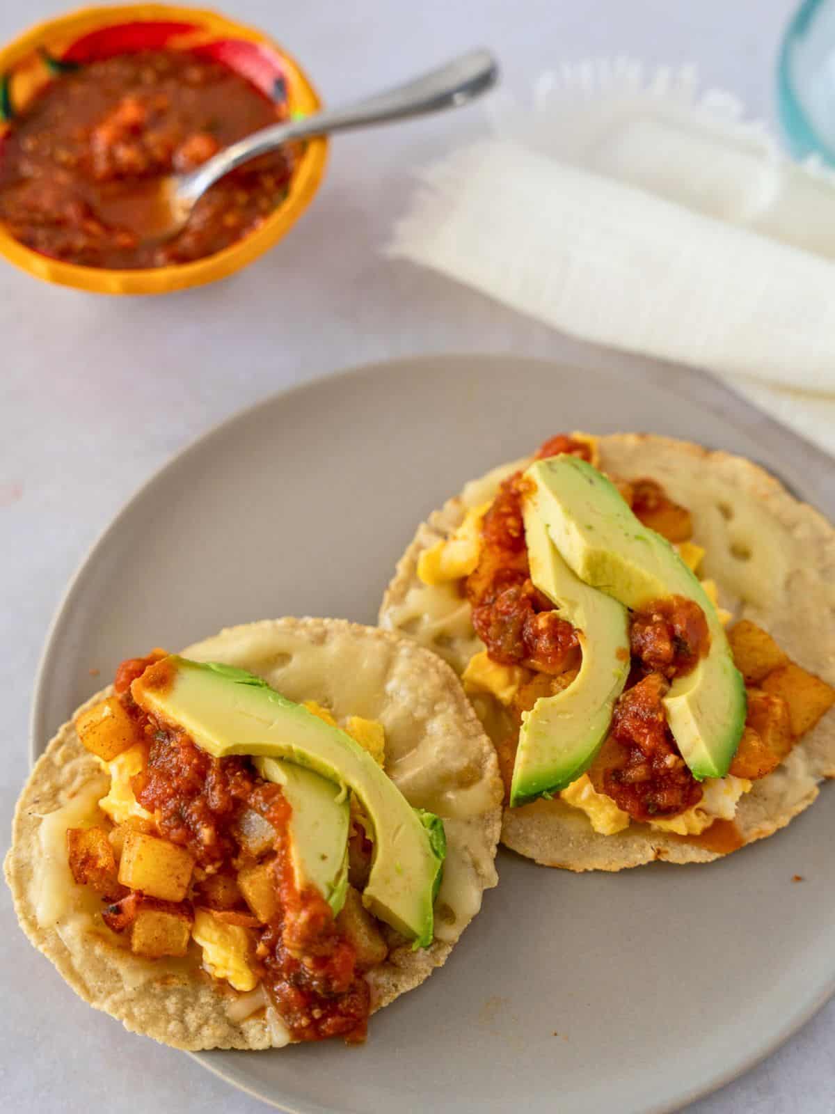 Potato and egg tacos topped with salsa and sliced avocado.