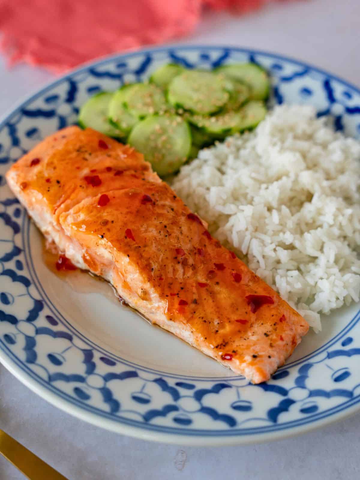 Sweet chili salmon on a plate with rice and cucumbers.