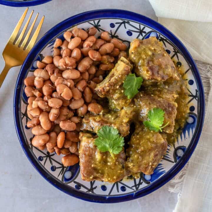 Feature image of costillas en salsa verde on a blue plate with beans.