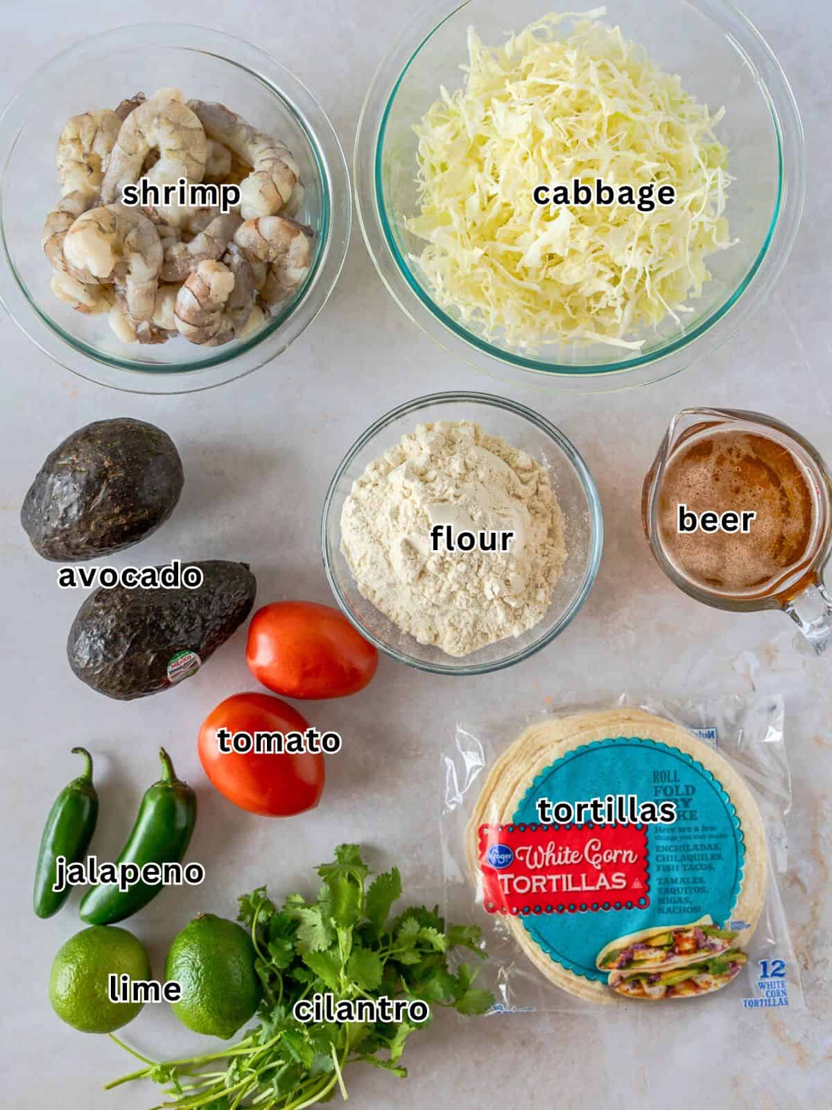 Ingredients with text- Shrimp, cabbage, avocado, flour, beer, tomato, jalapeno, lime, cilantro, and tortillas.